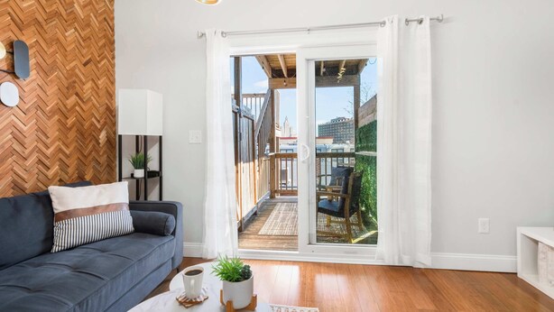 Een moderne woonkamer met een visgraat houten wand, een grijze bank, een salontafel en een schuifdeur die leidt naar een terras.