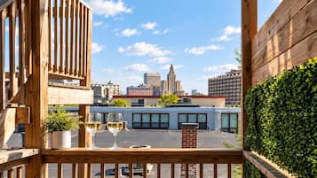 Ein Holzbalkon mit Blick auf die Stadt, zwei Gläsern Weißwein und einem Blumentopf.