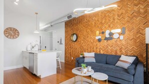 Een moderne woonruimte met een wand van visgraatmotief hout, een bank, een salontafel en een keuken met witte kastjes.