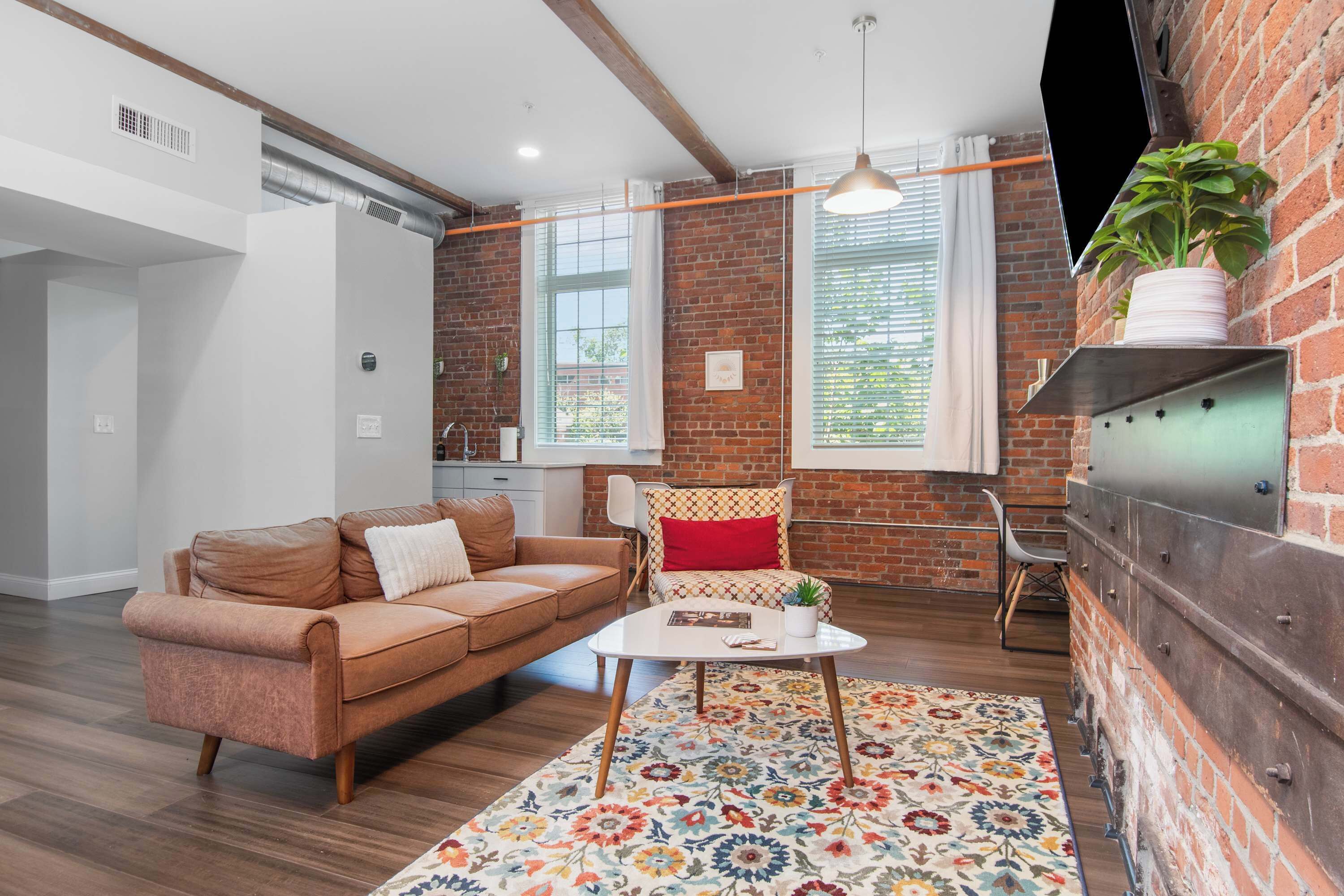Una sala de estar moderna con un sofá de cuero marrón, una mesa de centro blanca y un tapete floral colorido.