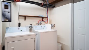 Un cuarto de lavandería con dos lavadoras de carga frontal, una máquina de cambio y tuberías visibles.