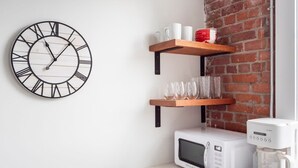 Una cocina con encimera blanca, microondas blanco, cafetera y un reloj con números romanos.