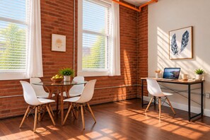 A room with a brick wall, a glass table, white chairs, a desk with a laptop, and a framed picture. - Jennifer’s Stylish Downtown Brick Foundry Escape (Providence)