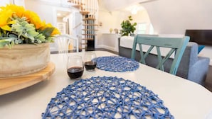 Een modern interieur met een ronde tafel, twee glazen rode wijn, een blauwe geweven onderzetter en een potplant met gele bloemen.