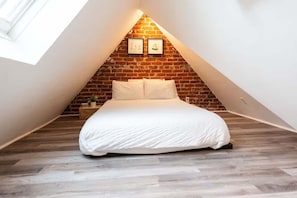 Une chambre avec un plafond en pente, un mur en briques et un lit.