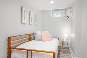 Une chambre à coucher avec un lit en bois, du linge de lit blanc, une petite table de chevet avec une lampe et des œuvres d’art encadrées accrochées au mur.
