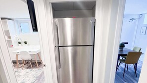 A modern kitchen with a stainless steel refrigerator, wooden flooring, and white cabinetry.