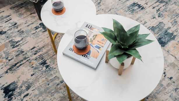 A round white table with a magazine, two glasses of beverage, and a small potted plant.