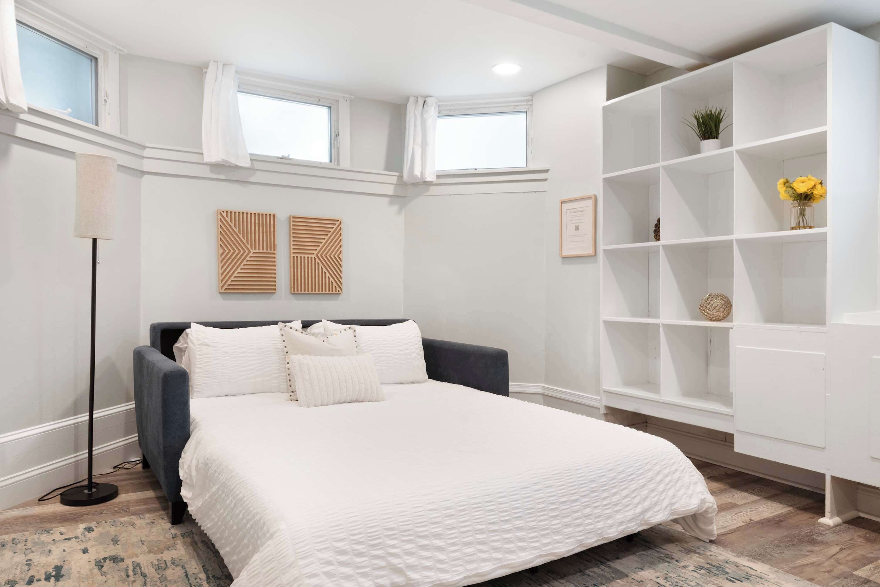 Un dormitorio con una cama, una lámpara de pie, una estantería y dos paneles decorativos en la pared.