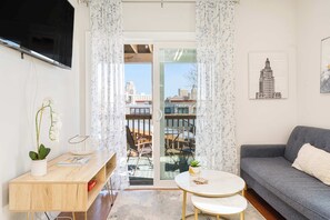 A living room with a sofa, a small round table, a TV mounted on the wall, and a view through a glass door. - Jennifer’s Getaway: Stunning Views & Private Deck (Providence)