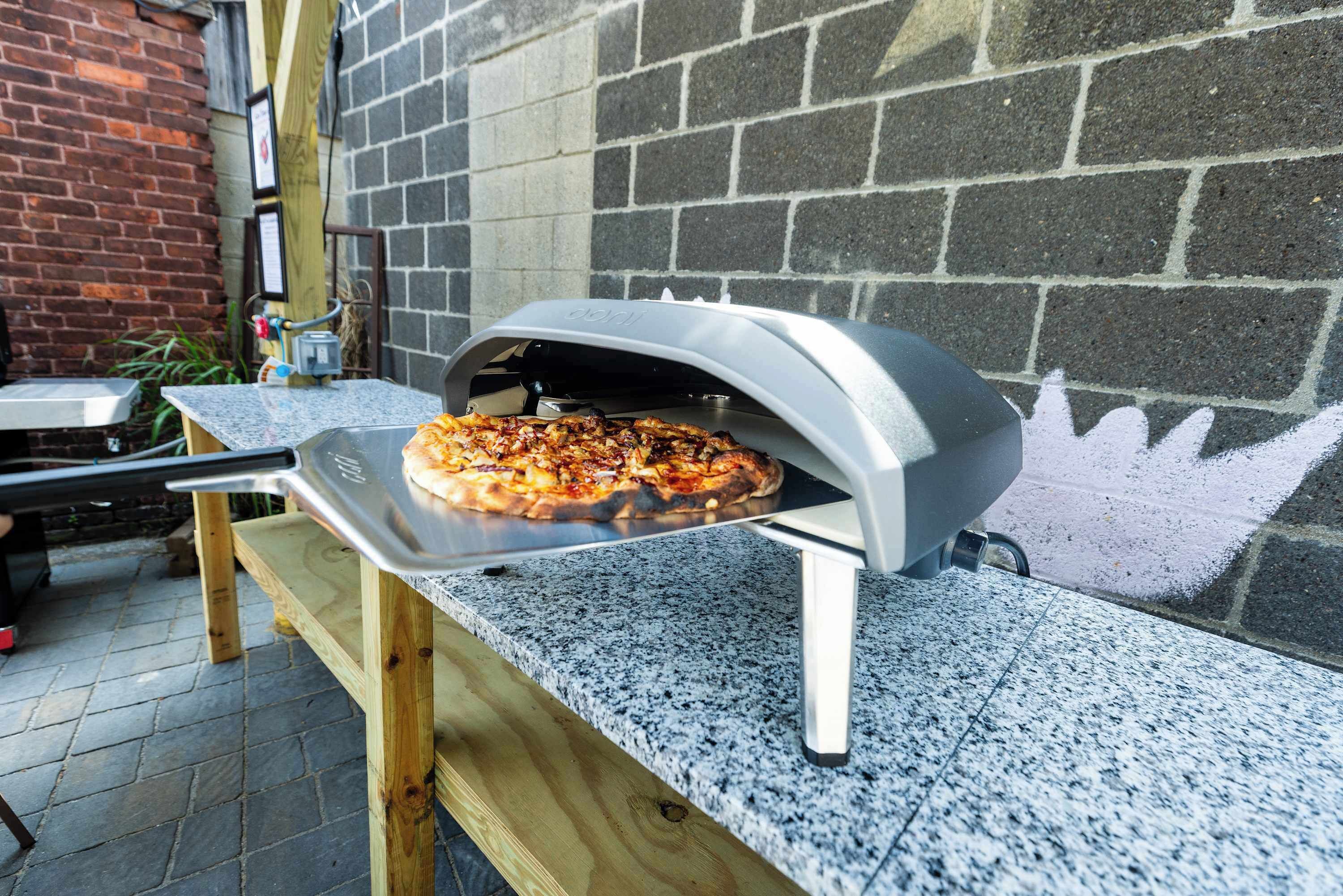 A pizza oven with a pizza inside, placed on a granite countertop.