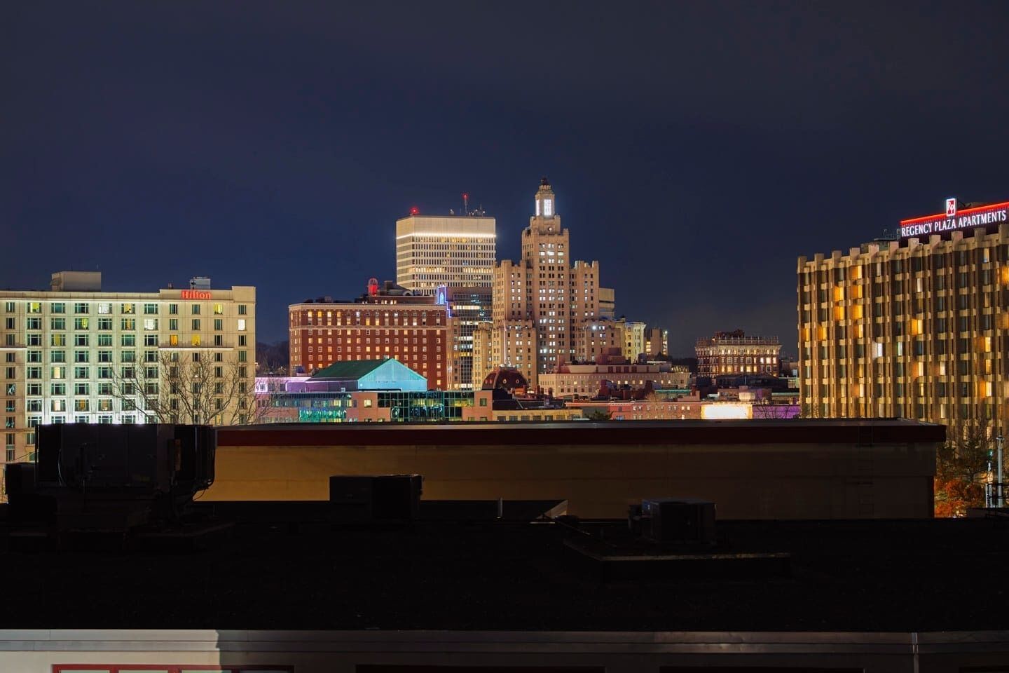 A city skyline at night with illuminated buildings, including a prominent hotel with a 'Hilton' sign.