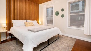 A bedroom with a wooden slatted ceiling, a bed with white bedding, two bedside lamps, and a window with blinds.