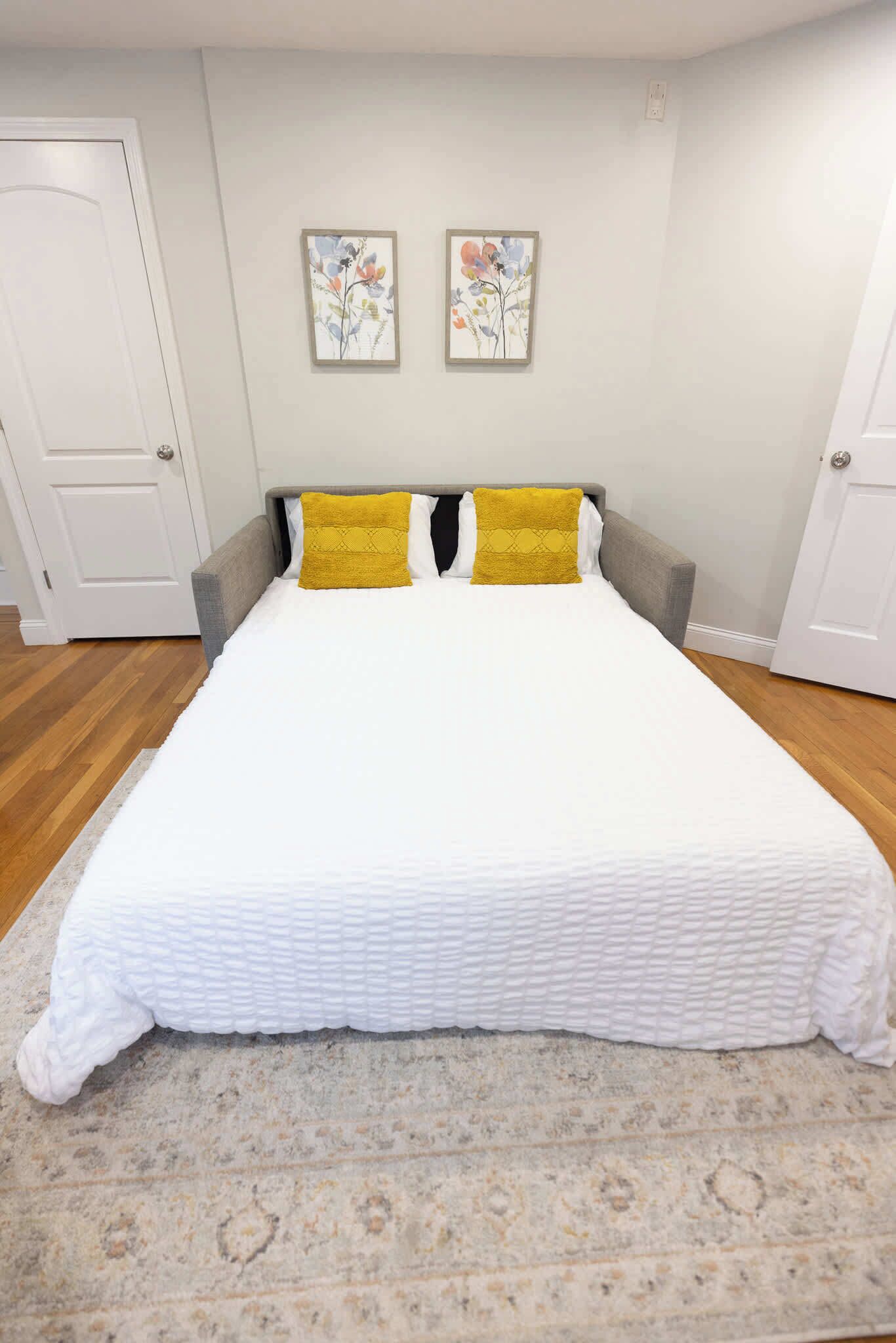 Un dormitorio con cama, dos almohadas, cabecera, alfombra y dos obras de arte en la pared.