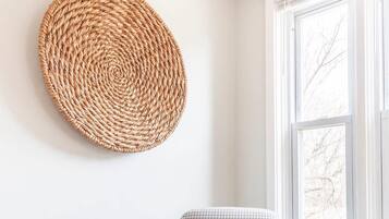 A chair with a houndstooth pattern, a woven wall hanging, and a window with a view of bare trees.