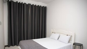 A neatly made bed with white bedding and a grey throw, a white headboard, and a black side table.