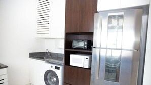 A compact kitchen with a washing machine, a microwave, and a stainless steel refrigerator.