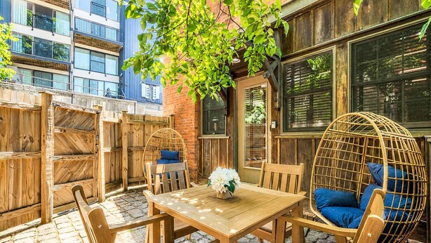 An outdoor patio with a wooden table and chairs, a wicker hanging chair, and a brick wall. - Jennifer’s Historic Riverfront Loft Private Entry (Providence)