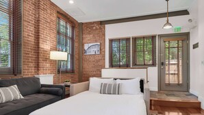 A hotel room with a brick wall, a bed, a sofa, and a door with an exit sign. - Jennifer’s Historic Riverfront Loft Private Entry (Providence)
