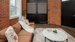 A room with a brick wall, a large black door, a brown sofa, a round marble table, and a window.