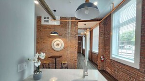 A kitchen with a brick wall, a round clock, a sink, and a window with blinds.