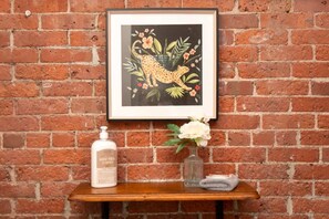 Una obra de arte enmarco con un leopardo y flores sobre un muro de ladrillo, una botella de leche de cabra y un florero con flores en un estante de madera.