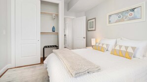 A bedroom with a bed, a closet, a chair, and a painting on the wall. - Jennifer’s Chic Apt w/ Downtown City Views Private Deck (Providence)