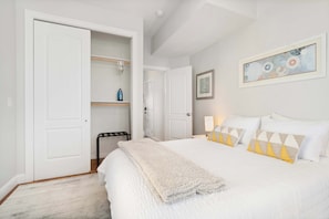 A bedroom with a bed, a closet, a chair, and a painting on the wall.