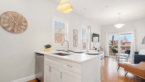 A modern kitchen with a wooden clock, white cabinets, and a central island with a sink. - Jennifer’s Chic Apt w/ Downtown City Views Private Deck (Providence)