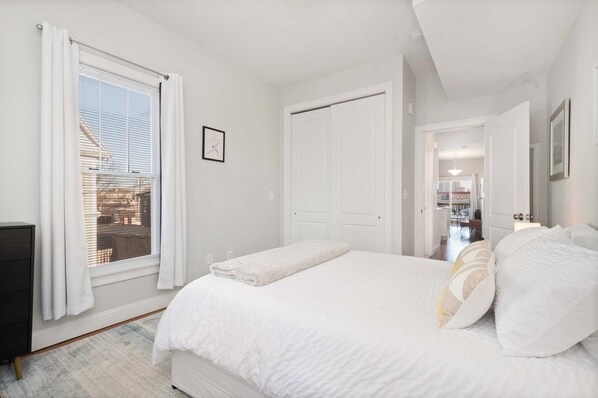 Un dormitorio con una cama grande, una ventana con persianas, una puerta y vistas a un edificio.