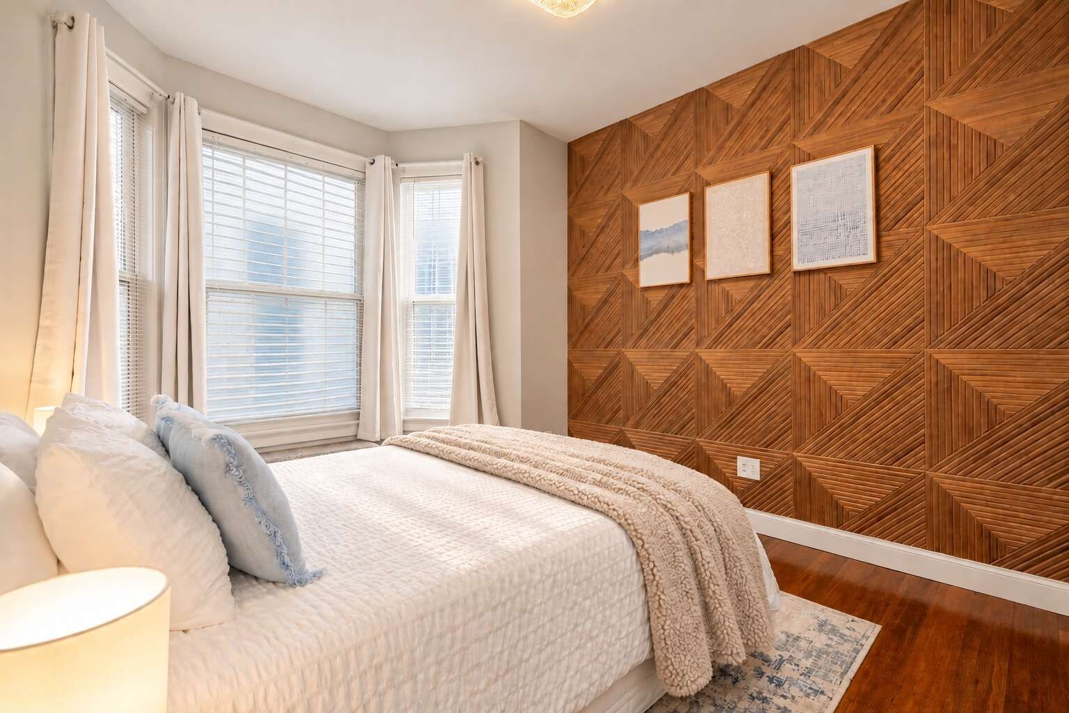 A bedroom with a bed, curtains, a wooden wall panel, and a rug.
