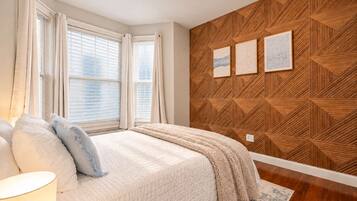 A bedroom with a bed, curtains, a wooden wall panel, and a rug.