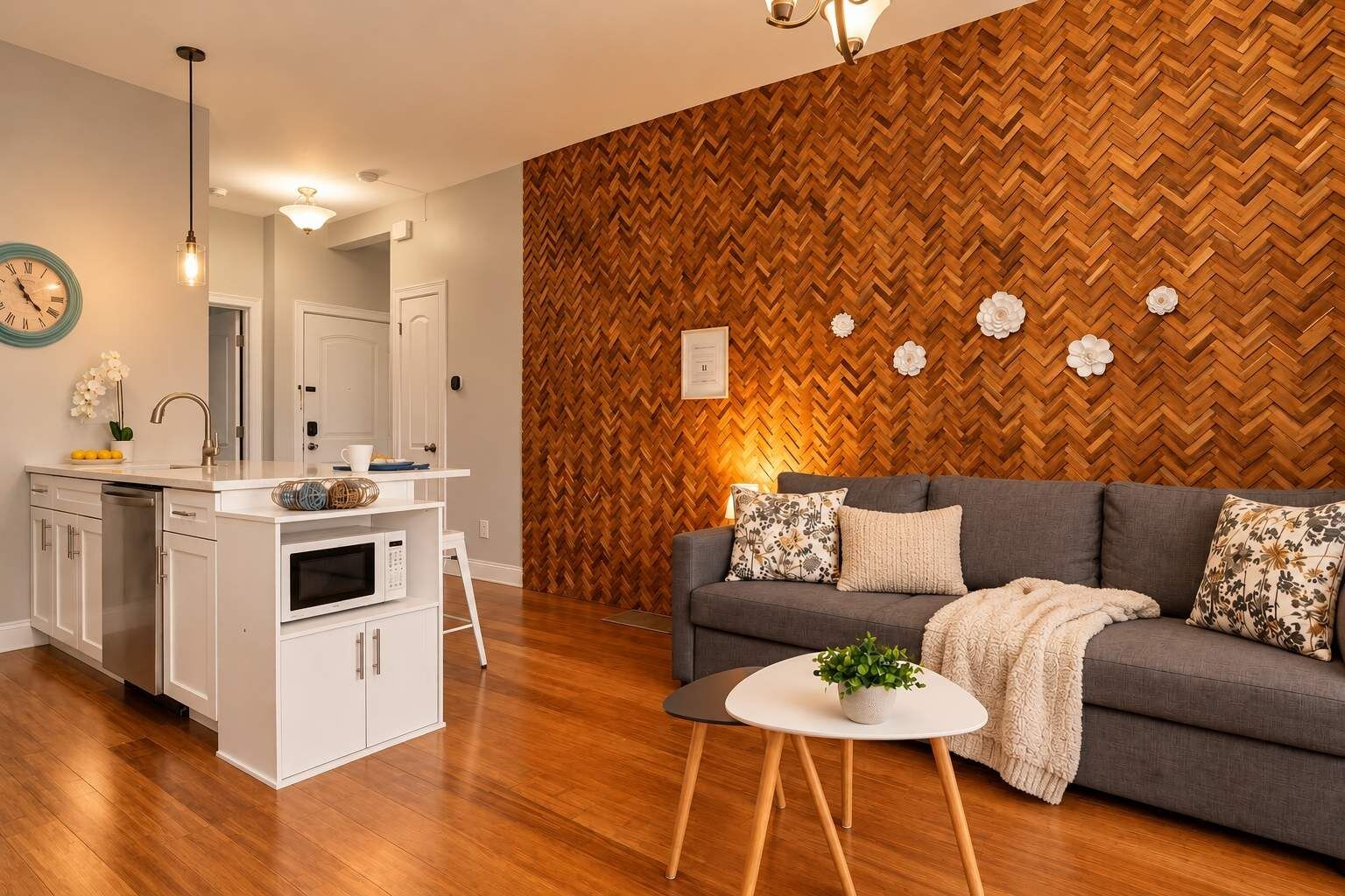 A modern living room with a herringbone-patterned wall, a grey sofa with floral cushions, and a white coffee table with a plant.