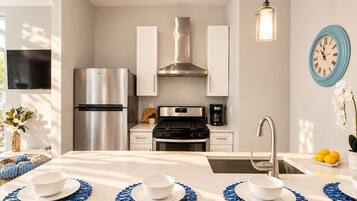 Een moderne keuken met roestvrijstalen apparatuur, een centraal eiland met blauwe placemats en een wandklok.