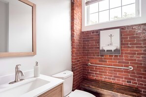 Une salle de bain avec un lavabo blanc, des toilettes, un miroir et un mur en briques.