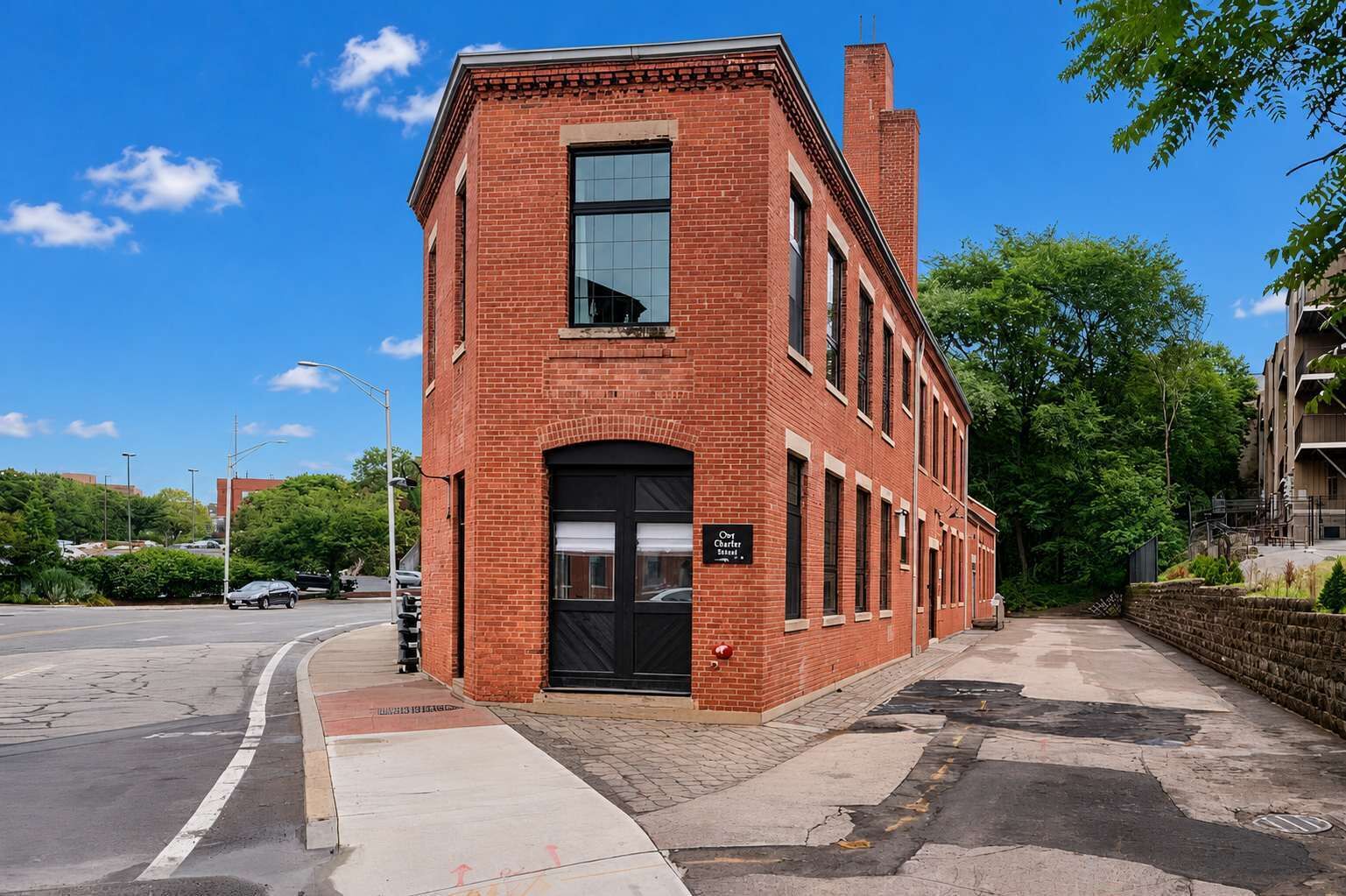 A red brick building with a black door and windows, located at a street corner with a sidewalk and trees.