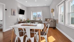 Una sala de estar moderna con comedor, un televisor de pantalla plana y un ventanal con vistas a la ciudad.
