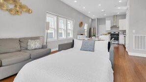 Un dormitorio moderno con una cama grande, un sofá gris y una kitchenette al fondo.