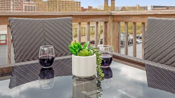 Una mesa de vidrio con dos sillas y una planta en maceta, ubicada en un balcón con vista a edificios.