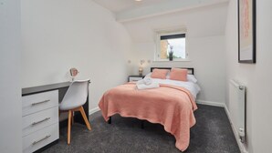 Ein Schlafzimmer mit Bett, Schreibtisch, Stuhl, Fenster und Heizkörper.