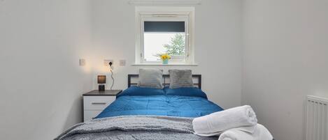 A bedroom with a bed, a nightstand, a window with a view, and a radiator.