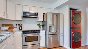 Une cuisine moderne avec des meubles blancs, des appareils en acier inoxydable et un lave-linge à chargement frontal de couleur rouge.