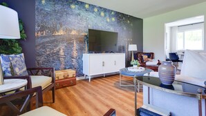 Un salon avec un grand tableau accroché au mur, un meuble blanc, un téléviseur et un canapé.