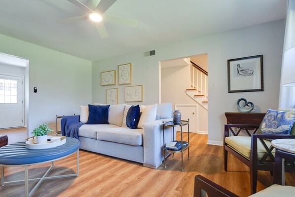 A living room with a light-colored sofa, a round coffee table, and a wooden floor. There is a staircase leading to an upper level.