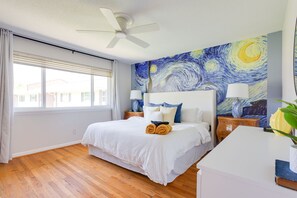 A bedroom with a large bed, two bedside tables, a ceiling fan, and a window with blinds.