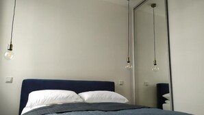 Un lit bien fait, avec une tête de lit sombre, une couverture matelassée et deux lampes de chevet.