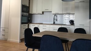 Une cuisine moderne avec des armoires blanches, une table à manger en bois et des chaises noires. Des suspensions noires sont fixées au-dessus du comptoir.
