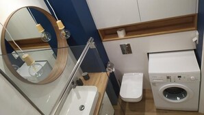 Une salle de bain moderne avec un lavabo en verre, un miroir rond, des toilettes et un lave-linge.