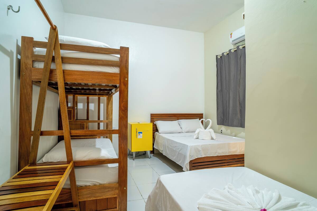 Une chambre avec des lits superposés, deux lits simples, une petite armoire jaune et une fenêtre avec des rideaux.