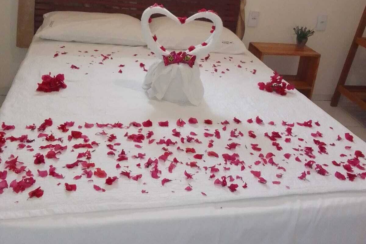 Un lit recouvert de pétales de rose, une composition en forme de cœur faite de pétales posée sur le lit, et deux ballons en forme de cœur accrochés au mur derrière le lit.